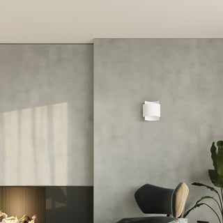 White wall lamp mounted on a textured grey wall above a dark chair and large houseplant.