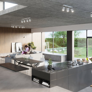 Open-plan room scene showing the white industrial spotlights mounted on a concrete ceiling above a kitchen island.