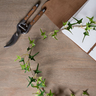 Artificial ivy garland styled on a wooden surface next to gardening shears and an open notebook.