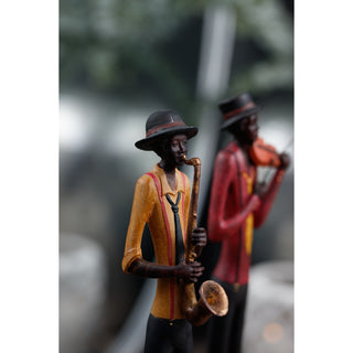 Saxophonist figurine in a hat and tie playing a saxophone, with another musician blurred in the background.