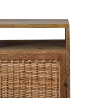 Close-up of the bedside table showing the open shelf above the woven rattan cupboard door.