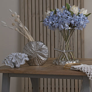 Light blue agapanthus bouquet styled with dried grasses and white coral on a wooden table against a slatted backdrop.