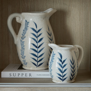 Large cream crackled jug vase with blue leaf design, shown next to a smaller matching jug on a book.