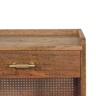 Close-up of the bedside cabinet's wooden top, drawer, textured brass handle, and woven cane shelf backing.