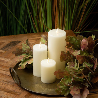 Three cream LED candles of different sizes styled on a metal tray with autumn foliage.