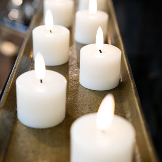 Six lit LED candles arranged closely in a long, narrow, textured metallic tray.
