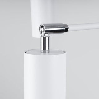 Detail of the polished chrome swivel joint mechanism above the white cylindrical lamp shade.