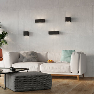 Styled living room scene showing four black wall lamps mounted above a white sofa on a light grey tiled wall.
