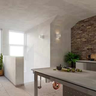 Styled shot showing two wall lamps in a bright kitchen with exposed brick and a metal island.