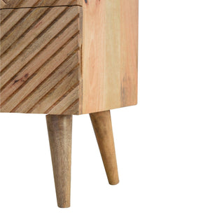 Close up of the bedside table's lower corner, showing the carved front, smooth side panel, and tapered wooden legs.
