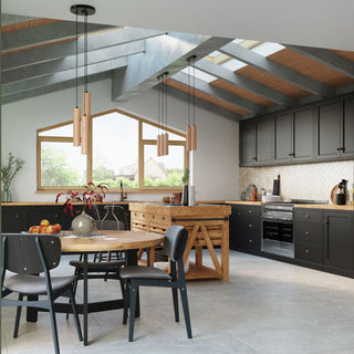 Two sets of wooden cylindrical pendants in a large kitchen with black units and skylights.