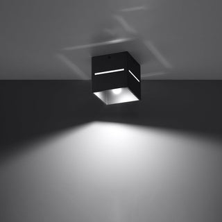 Black ceiling light cube showing light shining through side slits and casting patterns on the ceiling.