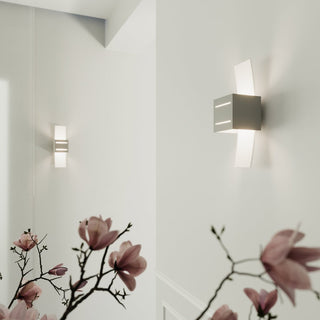Pair of grey wall lights installed sequentially in a white hallway, with blurred pink flowers in the foreground.