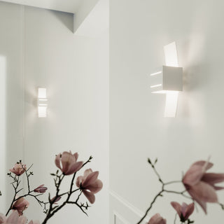 Two wall lamps installed in a white corridor corner, seen through blurred branches of pink magnolia flowers.