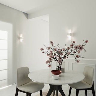 Pair of wall lamps illuminating a dining area with a round table, chairs, and pink floral display.