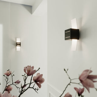 Pair of black wall lights illuminating a white corridor, viewed through branches of pink blossoms.
