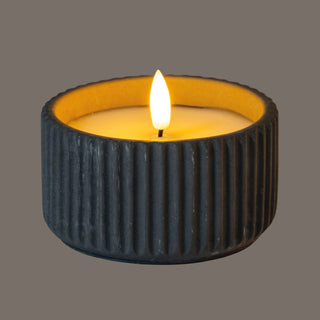 Angled view of the small LED candle in a ribbed grey holder, highlighting the yellow glow on the inner rim.