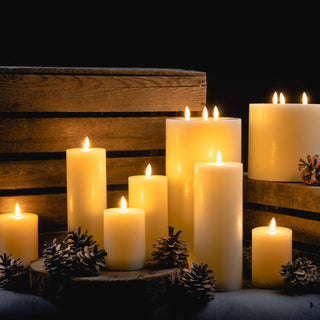 Group of cream LED candles styled with pine cones and rustic wooden crates in a dark setting.