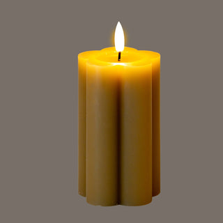 Fluted stone LED candle glowing yellow at the top, with a bright white faux flame, on a solid grey background.