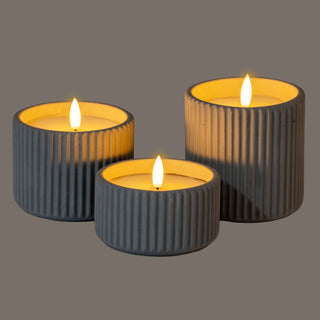 Three ribbed grey LED candles in different sizes, illuminated to show the textured surface and warm glow.