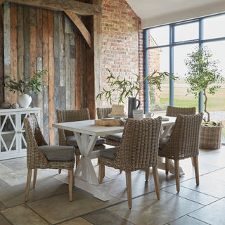 The matte white vase sits on a white cabinet in a rustic dining room setting next to reclaimed wood.