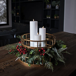 Festive berry picks and greenery arranged around a gold mirrored candle tray on a dark wooden table.