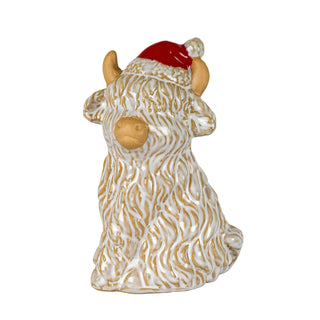 Ceramic Highland cow ornament wearing a red Santa hat, glazed white and beige, shown front-on.