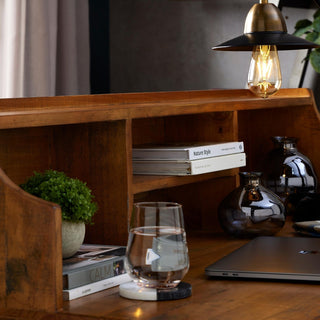 Miniature hebe in grey pot on a wooden bureau shelf, styled with books and dark glass vases.