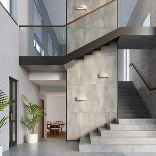 Three concrete wall lights mounted vertically beside a staircase in a large, modern architectural interior.
