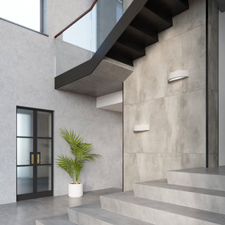 Two concrete lights mounted on a grey panelled wall beside a modern black and glass staircase.