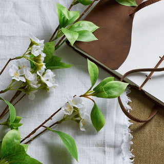 Close-up of artificial mock orange flowers and bright green leaves resting on a leather-bound notebook.
