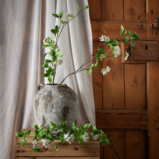 Artificial mock orange branches displayed in a rustic grey urn on a wooden crate.
