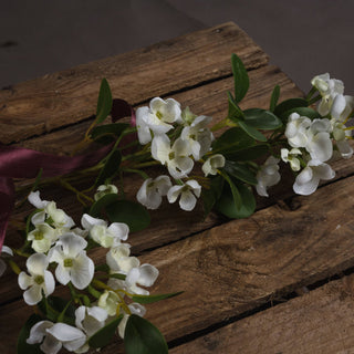 Close-up detail of white artificial mock orange flowers and green leaves on rustic wooden planks.