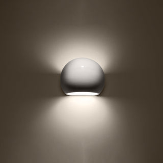 Glossy white globe wall light showing the warm upward and downward light effect on a dark wall.