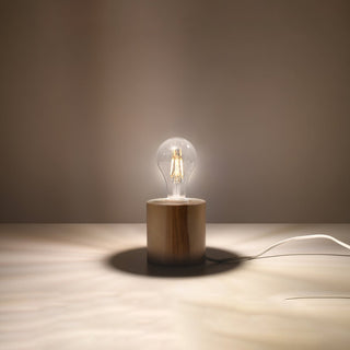 The natural wood lamp lit in a dark setting, casting a warm pool of light and shadow on the surface.