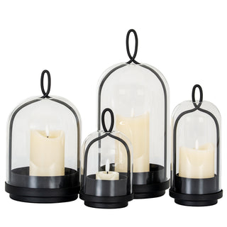 Four black metal and glass cloche candle holders of varying sizes, each with a lit candle.