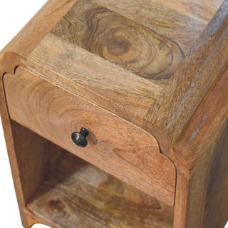 Angled close-up showing the nightstand's top surface wood grain, curved edges, and the scalloped joint above the drawer.