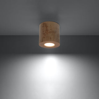 Cylindrical wooden ceiling light switched on, casting a bright downward beam onto a dark grey wall.