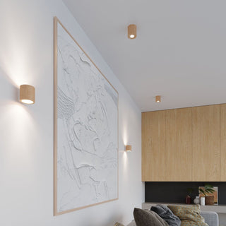 Cylindrical wood fixtures used as ceiling downlights and wall up/downlights in a modern room setting.