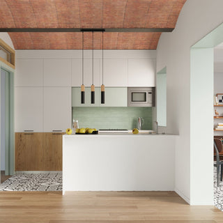 Pendant lamp hanging over a white kitchen island with a green tiled splashback and vaulted brick ceiling.