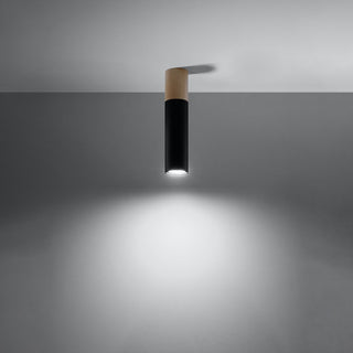 Cylindrical black and wood ceiling lamp switched on, casting a bright, focused beam of light onto a dark wall.