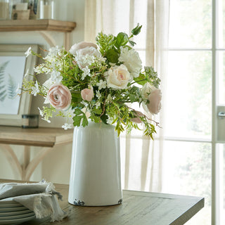 Pastel pink ranunculus used in a mixed floral arrangement on a wooden dining table by a bright window.
