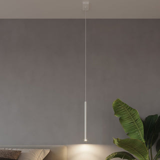 Single white cylindrical pendant drop suspended long in a styled bedroom setting next to a large plant.