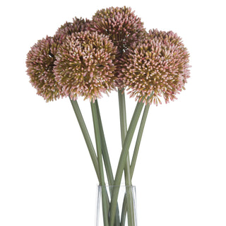 Five artificial pink allium flowers grouped together with green stems in a transparent glass vase.