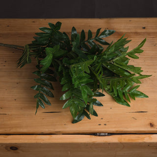 Artificial green foliage bunch resting on a light brown wooden surface, showing leaf texture.