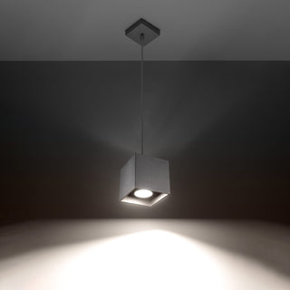 Grey textured cube pendant lamp hanging, showing the bright downward light beam against a dark background.