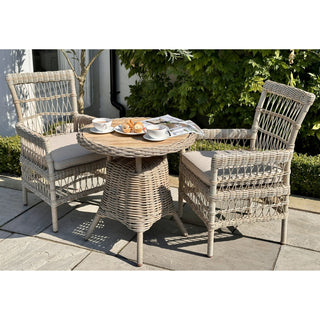 Two light grey rattan chairs and a matching table set for tea on a sunny patio.