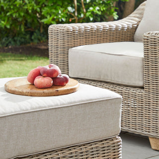 Close-up of the beige footstool cushion used as a side table, holding a wooden board with peaches.