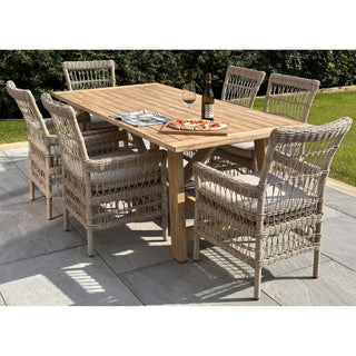 Six light grey rattan dining chairs with beige cushions surrounding a wooden table outdoors.