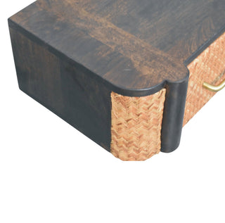 Close-up of the dark wood corner detail where the frame meets the light herringbone rattan drawer front.